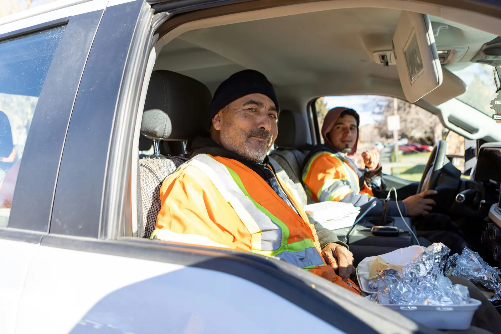 Two fleet workers in high-visibility jackets smiling from inside a truck cab